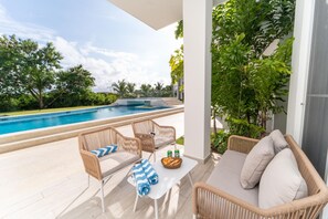 A poolside area with wicker furniture, a table, and a view of a swimming pool and greenery.