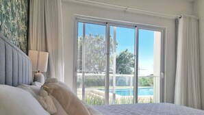 Un dormitorio con una cama grande, vista a una piscina y un ventanal corredera.
