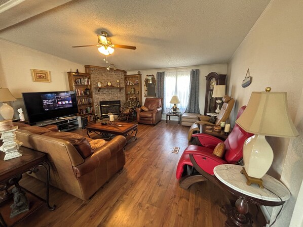 A living room with a fireplace, leather furniture, a television, and a ceiling fan.