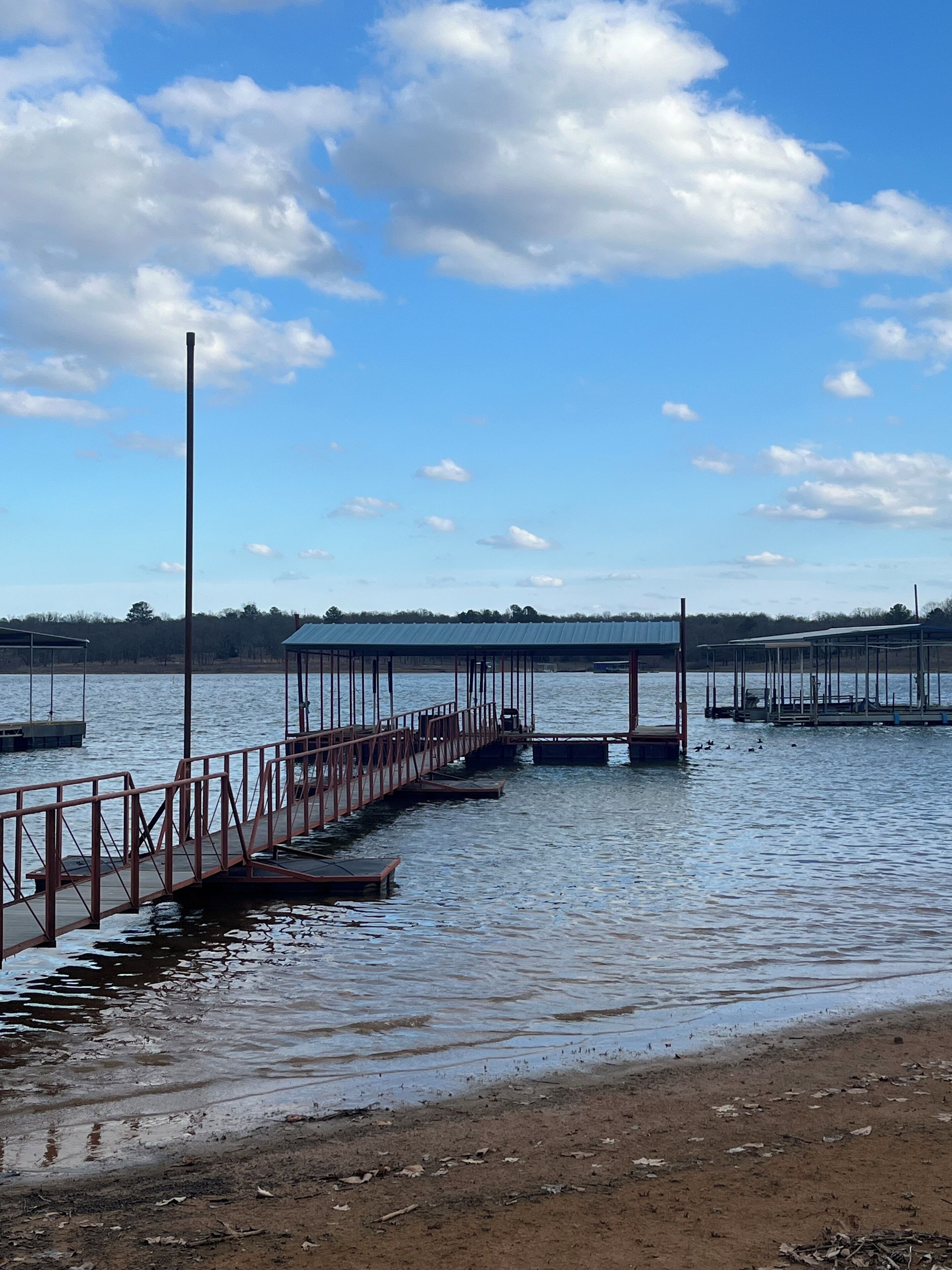 A waterfront dock with a metal railing, a wooden walkway, and a clear sky with clouds.