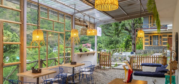 A restaurant with large windows, blue chairs, and hanging wicker lamps. - Zostel Homes Tirthan - Gushaini (Banjar)