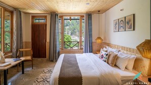 Un dormitorio con techo de madera, una cama grande con muchas almohadas, un escritorio con una computadora portátil y una ventana con cortinas.