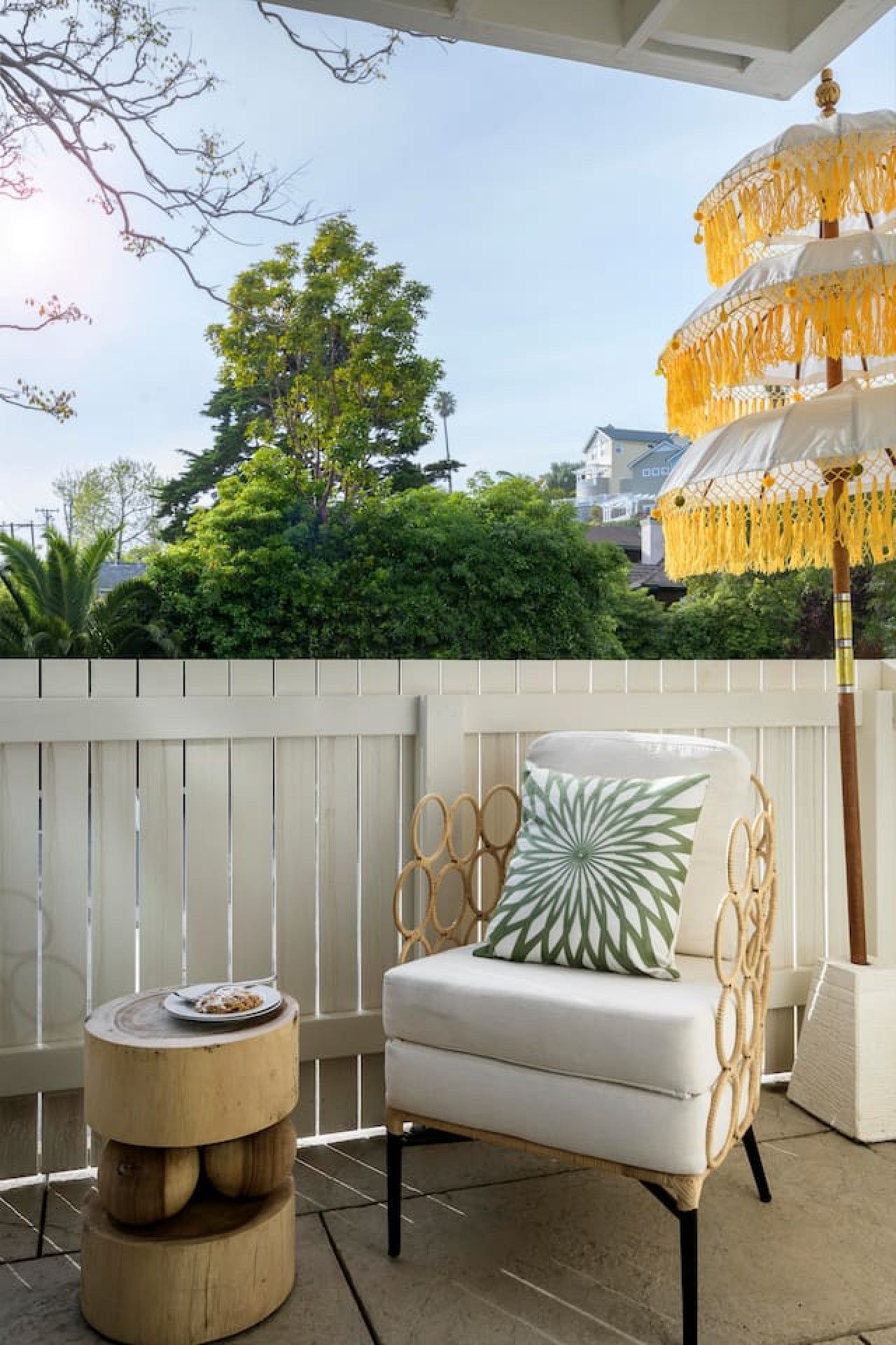 A patio with a white chair, a round wooden table, and a yellow umbrella.