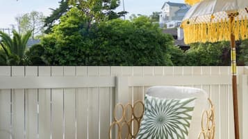 A patio with a white chair, a round wooden table, and a yellow umbrella.