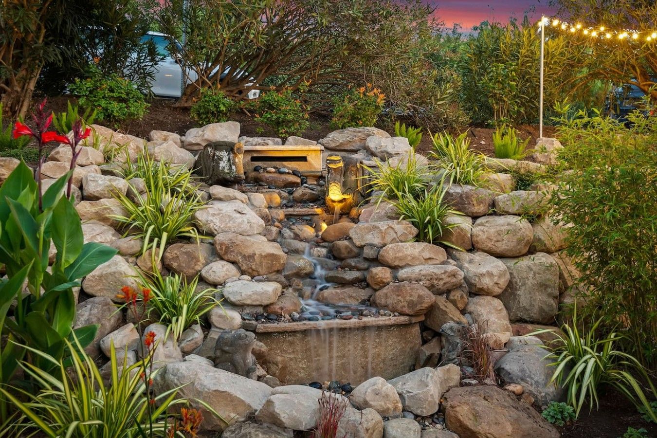 A garden with a rock waterfall, a wooden bench, and various plants.