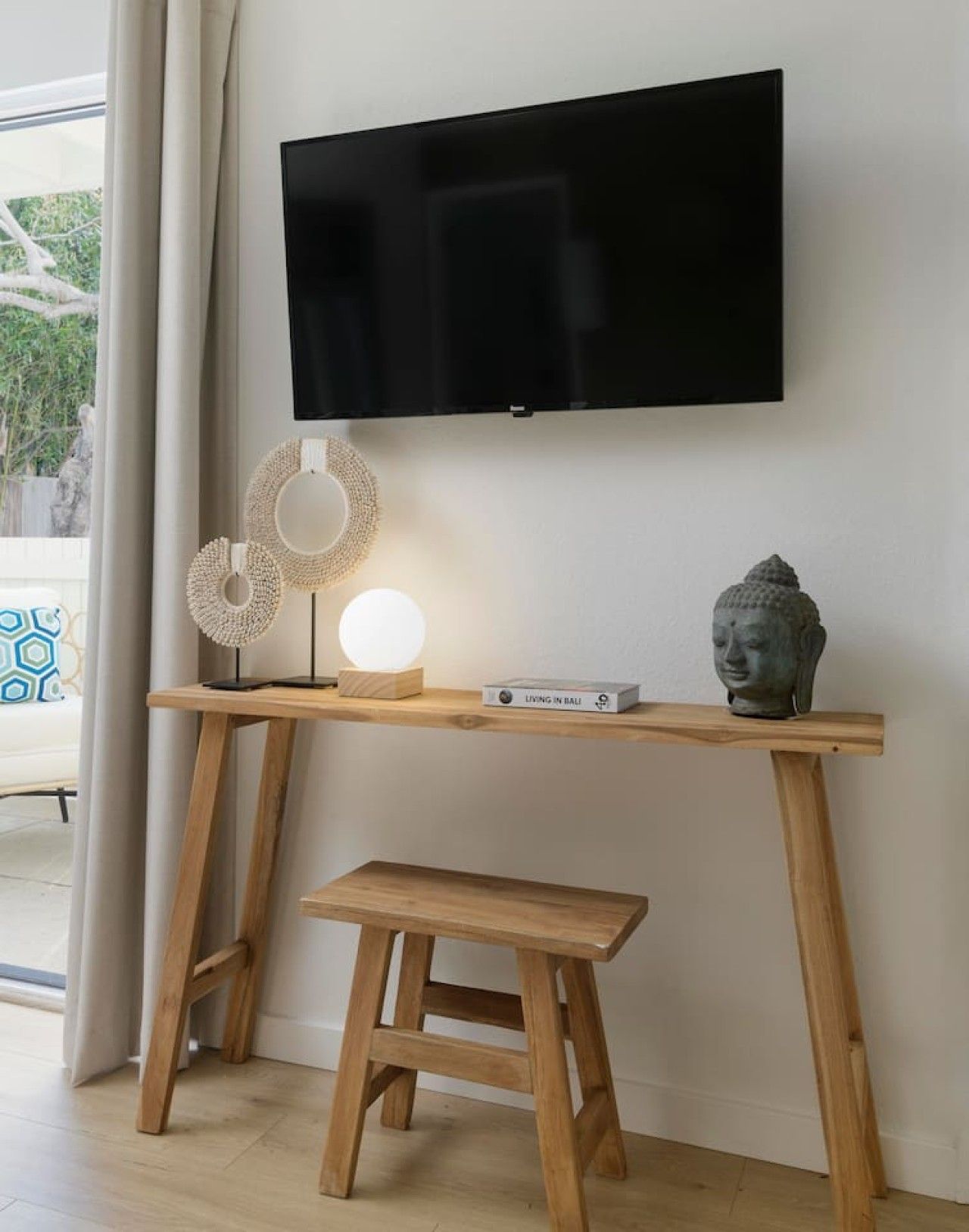 Een houten bureau met daarboven een televisie, een klein krukje, en decoratieve voorwerpen zoals een Boeddhabeeld en een lamp.