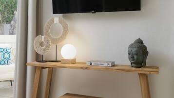 Een houten bureau met daarboven een televisie, een klein krukje, en decoratieve voorwerpen zoals een Boeddhabeeld en een lamp.