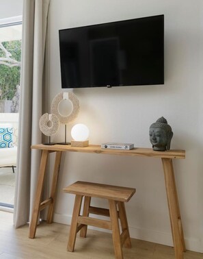 Ein Holztisch mit einem darüber angebrachten Fernseher, ein kleiner Hocker und dekorative Gegenstände, darunter eine Buddha-Statue und eine Lampe.