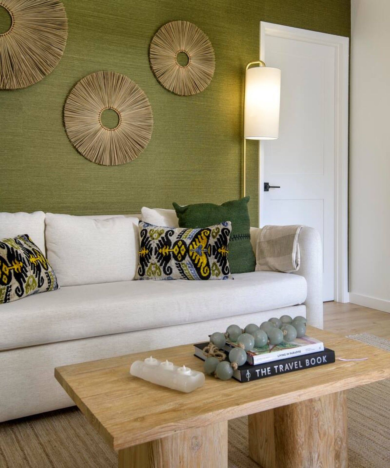 Een woonkamer met een witte bank, gestreepte kussens, een houten bijzettafeltje met boeken en kaarsen, en wanddecoratie.