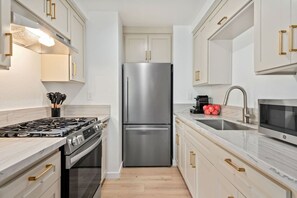 Una cocina moderna con electrodomésticos de acero inoxidable, armarios blancos y encimera de mármol.