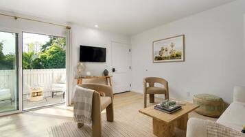 Een moderne woonkamer met een grote schuifpui naar een balkon, een flatscreen televisie aan de muur en een houten salontafel met boeken.
