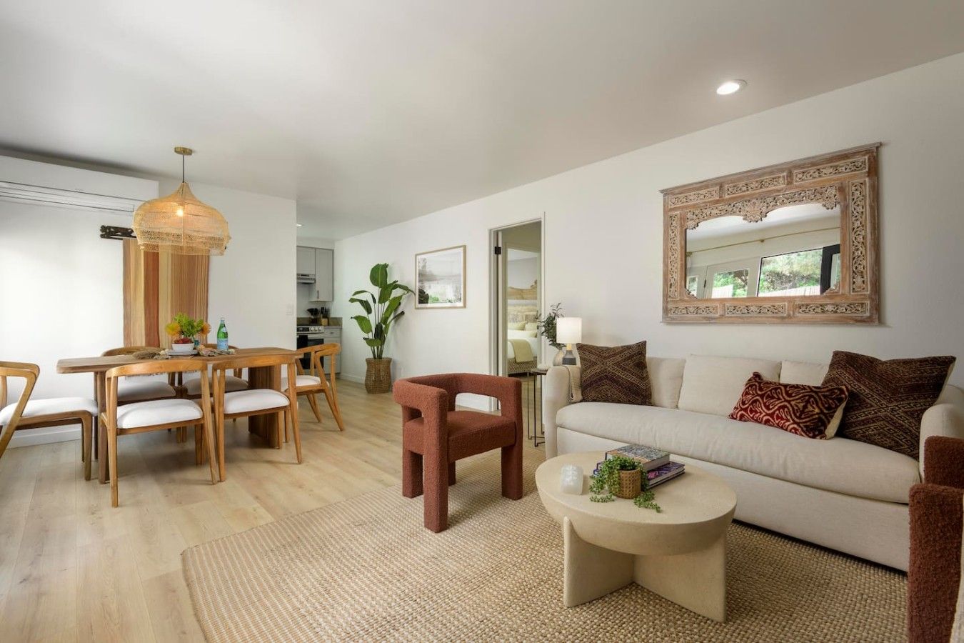 A modern living room with a dining area, a sofa set, a coffee table, and a large mirror.