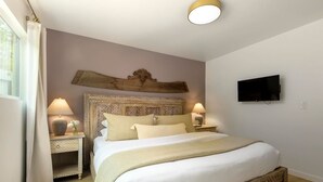 Een slaapkamer met een groot bed, twee nachtkastjes met lampen, een televisie aan de muur en een decoratief hoofdeinde.