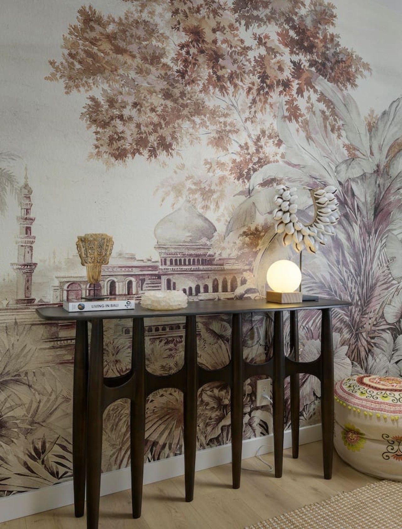 Een kamer met een muurschildering van een traditioneel gebouw en bomen, een tafel met een lamp en een decoratieve schaal.