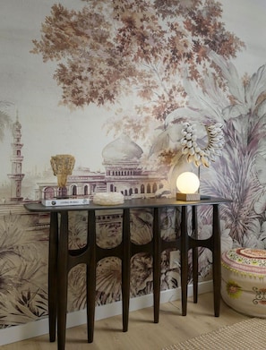 Una habitación con un mural que muestra un edificio tradicional y árboles, una mesa con una lámpara, y un cuenco decorativo.