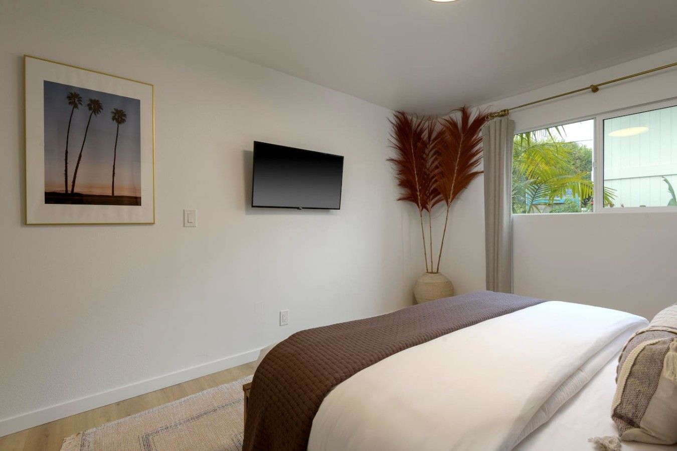 A bedroom with a bed, a flat-screen TV, a framed picture, and a window with curtains.