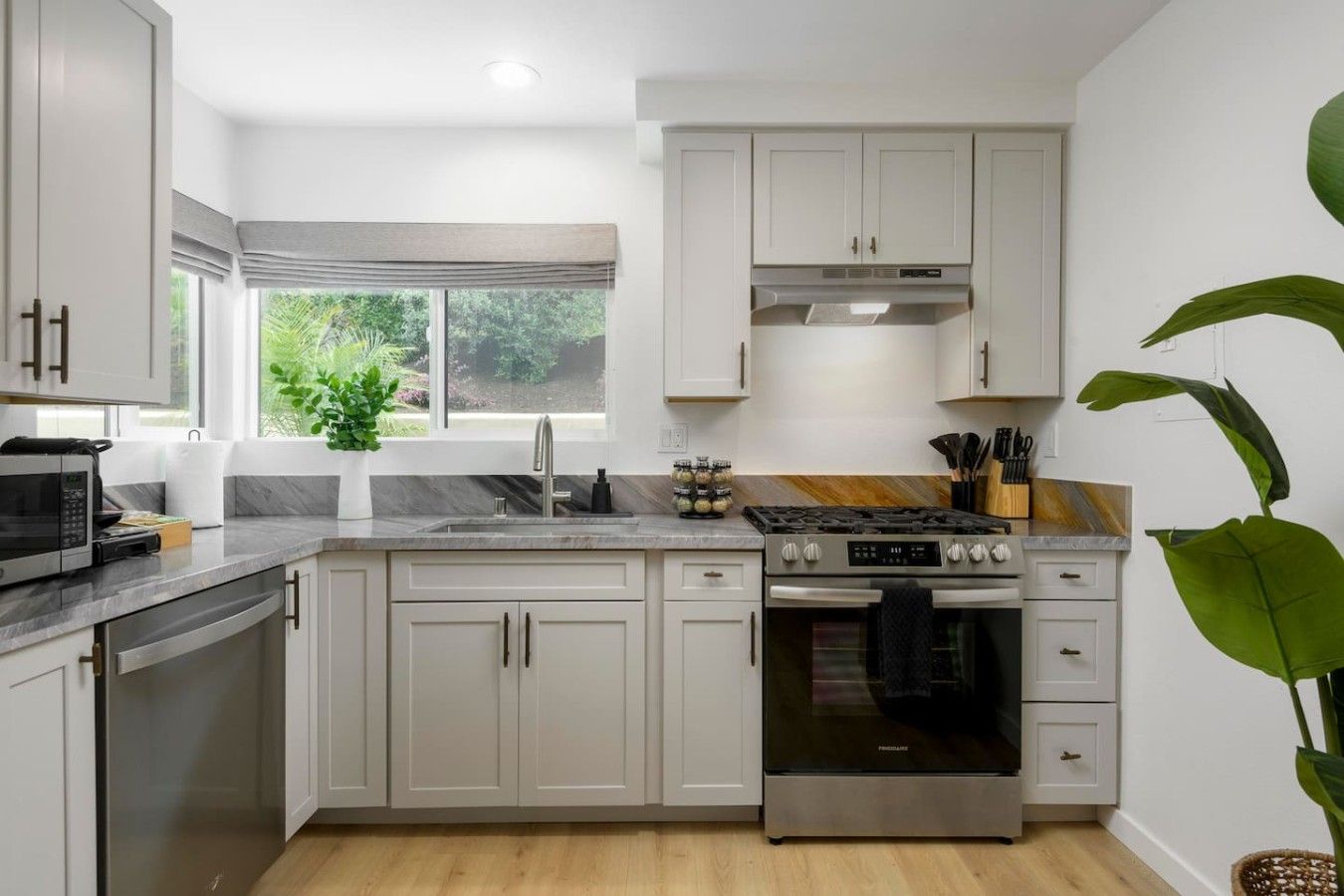 Une cuisine moderne avec des meubles blancs, une cuisinière en acier inoxydable et une fenêtre donnant sur un paysage verdoyant.
