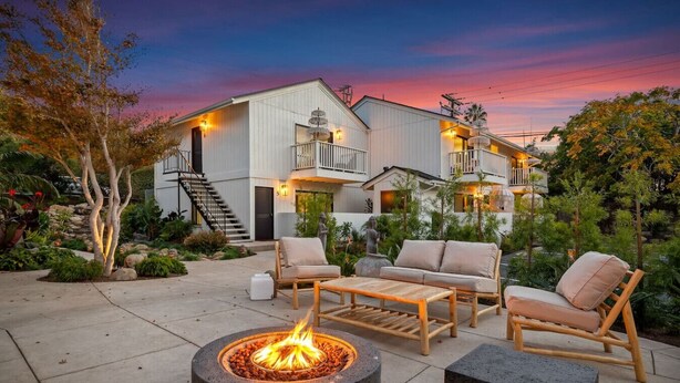 A modern outdoor patio with a fire pit, lounge chairs, and a staircase leading to a building.