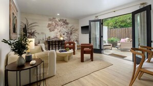 A spacious living room with a large window, a sofa, a coffee table, and a TV mounted on the wall.