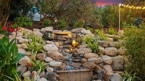 A garden with a rock waterfall, a wooden bench, and various plants.