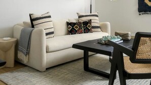 A modern living room with a sofa, coffee table, and a round table with chairs. There are decorative wall art pieces above the sofa and a floor lamp.
