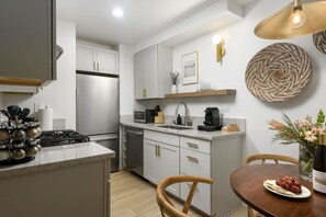 A modern kitchen with a built-in stove, microwave, and sink. There is a dining area with a wooden table and chairs. - Bali Home | SB Beaches (Summerland)