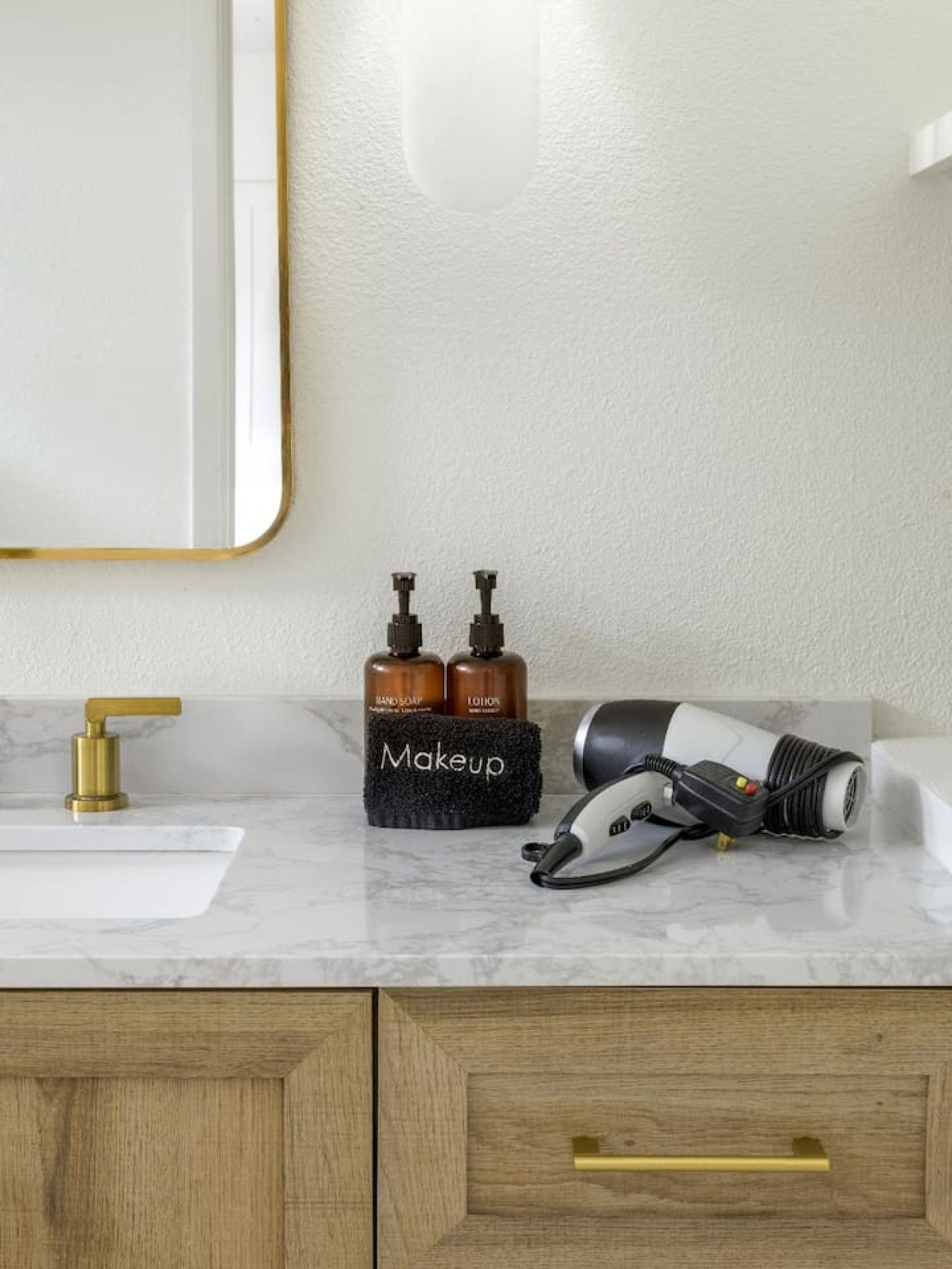 Un meuble-lavabo pour la salle de bain avec un plan de toilette en marbre, un robinet doré, un organiseur de maquillage et un sèche-cheveux.
