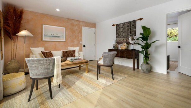 A living room with a sofa, two armchairs, a coffee table, a rug, a lamp, a plant, and a wall-mounted tapestry.