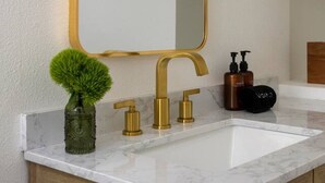 A bathroom with a marble sink, gold faucets, a mirror, and a small green plant.