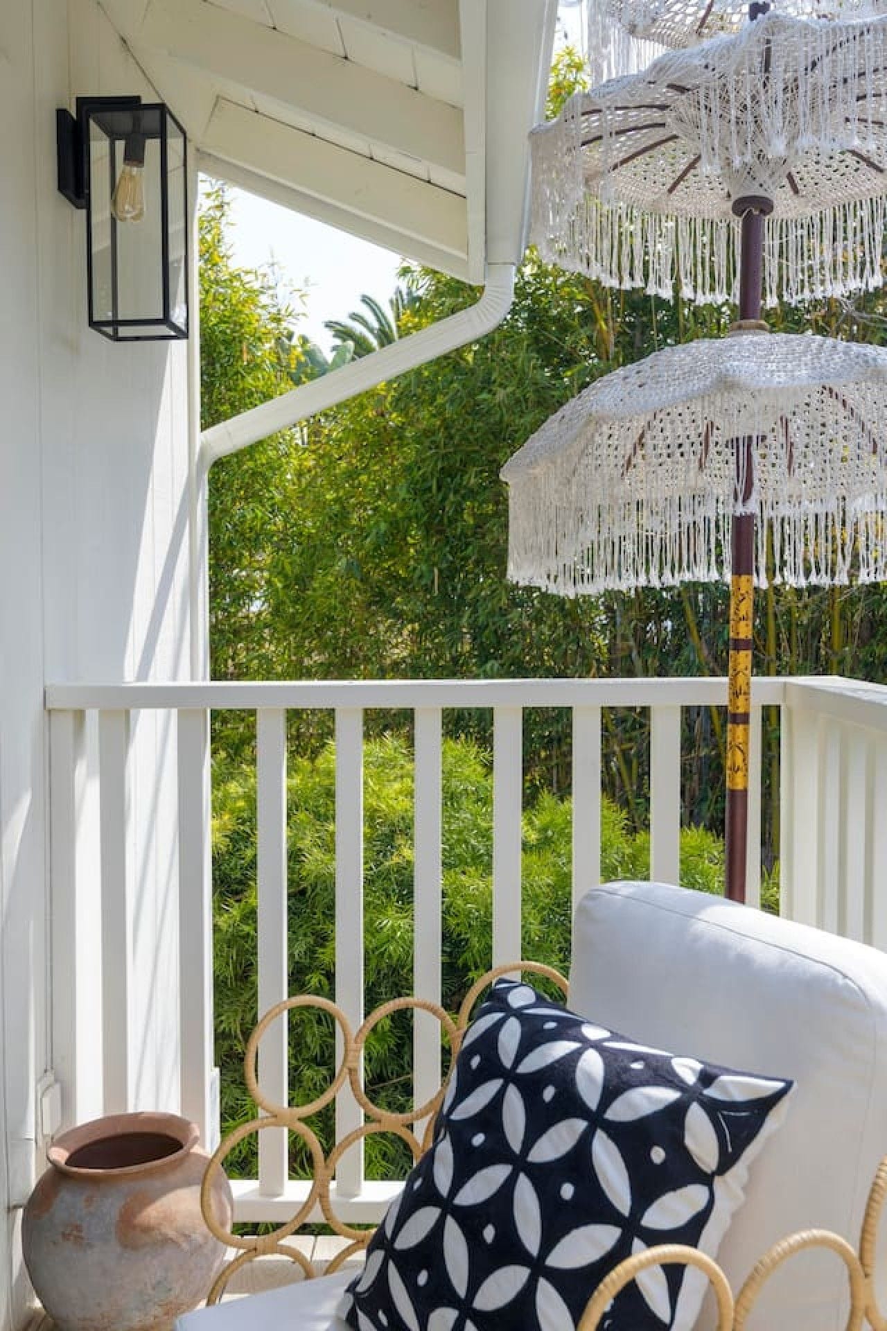 Een balkon met witte reling, een rieten stoel, een gekleurd kussen en een decoratieve parasol.