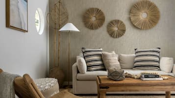 Een woonkamer met een bank, kussens, een salontafel, een vloerlamp en decoratieve wandobjecten.