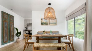 A dining area with a wooden table, woven bench, and a hanging light fixture. - Group-Friendly | Tranquil Oasis (Summerland)