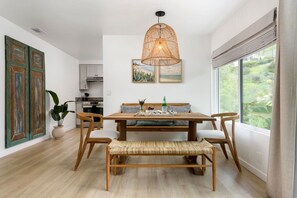 Un comedor con mesa de madera, banca tejida y lámpara colgante.