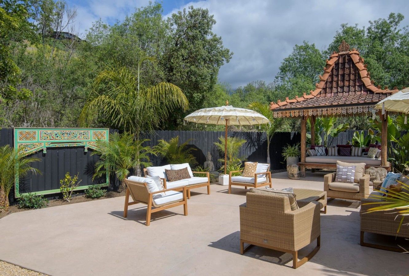 An outdoor patio area with seating arrangements, including sofas and chairs, and a decorative structure with a tiled roof.