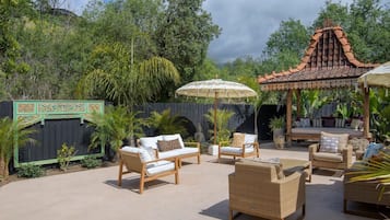 An outdoor patio area with seating arrangements, including sofas and chairs, and a decorative structure with a tiled roof.