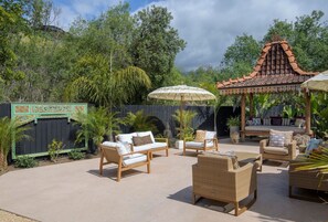Un patio al aire libre con arreglos de asientos, incluyendo sofás y sillas, y una estructura decorativa con techo de tejas.