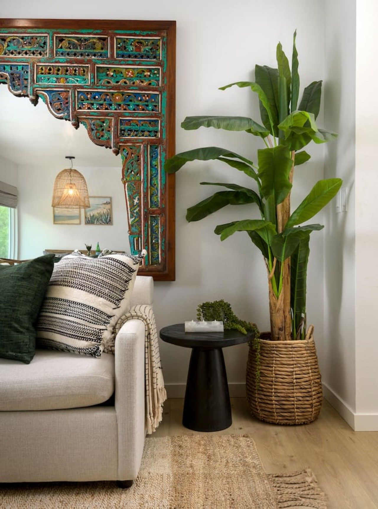 Een woonkamer met een bank, een grote plant, een decoratief paneel en een bijzettafeltje.