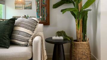 Een woonkamer met een bank, een grote plant, een decoratief paneel en een bijzettafeltje.