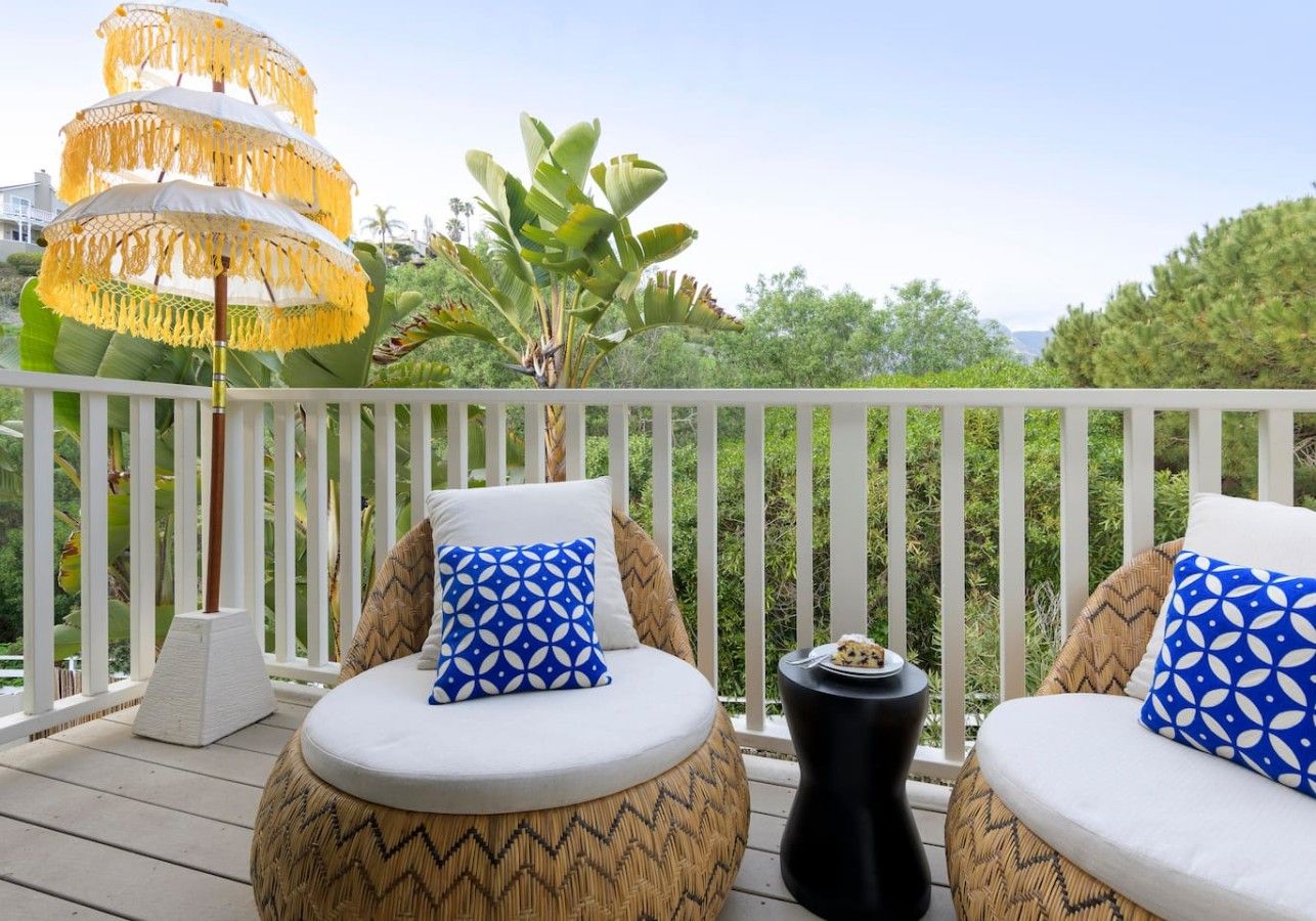 A balcony with two round cushioned seating areas, each with a patterned pillow, a small side table, and a decorative umbrella.