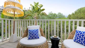 A balcony with two round cushioned seating areas, each with a patterned pillow, a small side table, and a decorative umbrella.