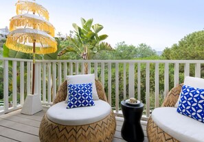 A balcony with two round cushioned seating areas, each with a patterned pillow, a small side table, and a decorative umbrella.