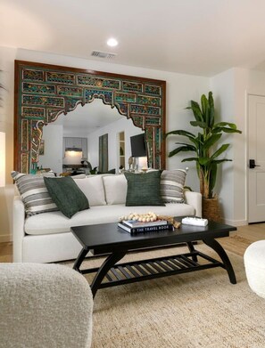 Una sala de estar con un sofá blanco, una mesa de centro y un espejo decorativo grande con un marco ornamentado.
