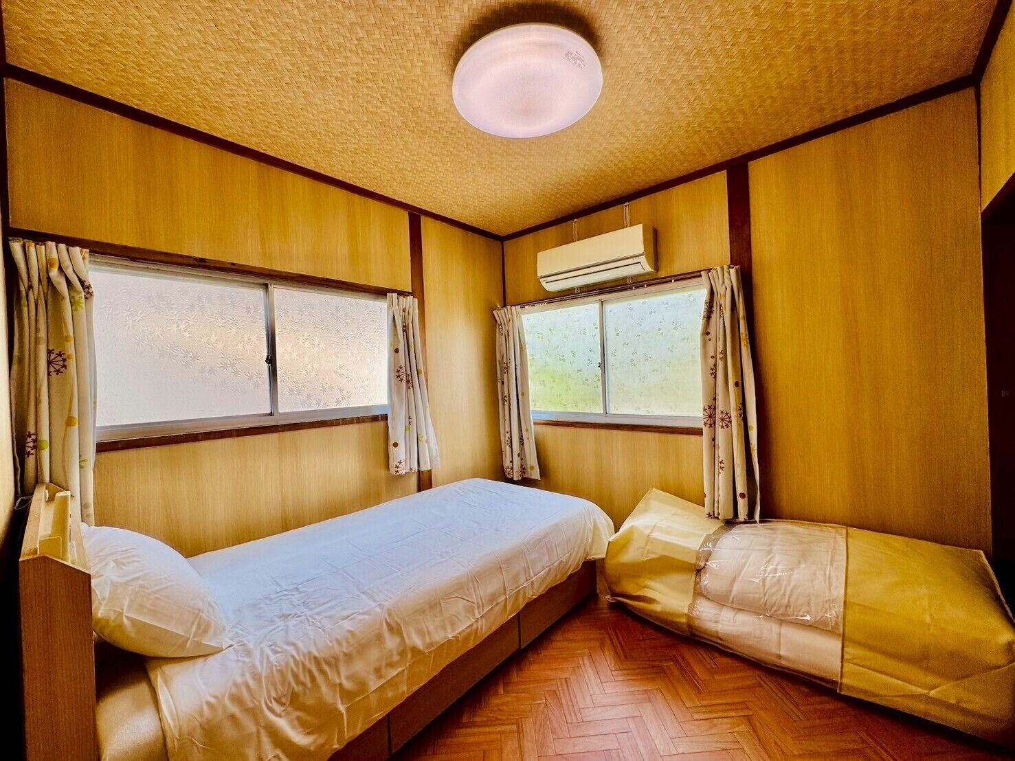 A compact room with two beds, wooden walls, and a ceiling fan.
