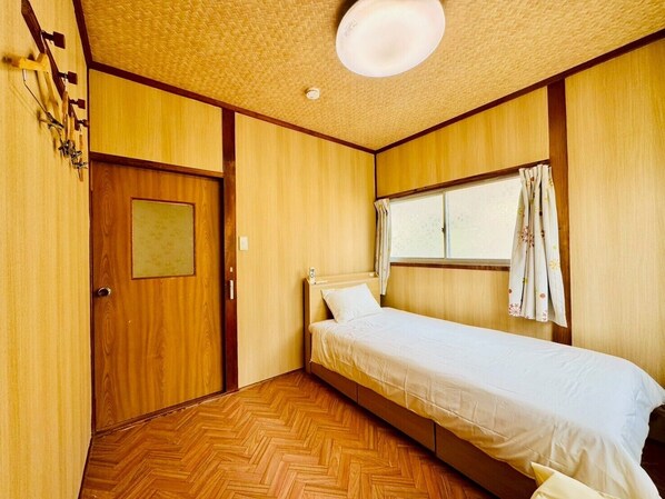 Une petite chambre avec un lit simple, des murs en bois et un parquet disposé en motif à chevrons.