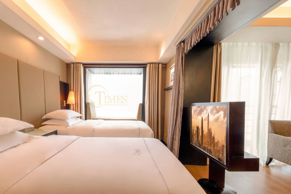 Une chambre d’hôtel avec deux lits, une télévision et une grande fenêtre avec des rideaux.