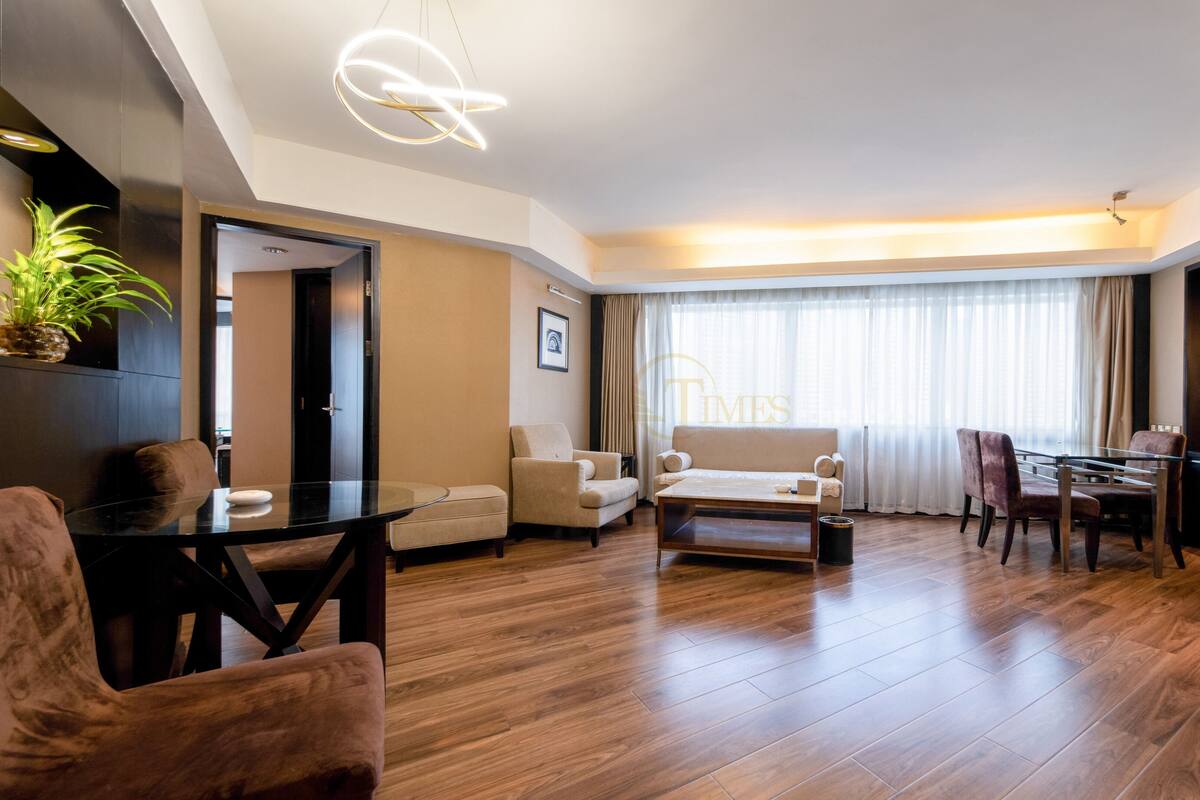 Un salon moderne avec une table basse en verre, deux canapés, une table à manger avec des chaises et une grande fenêtre avec des rideaux.