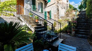 A stone building with a staircase leading to a wooden door. There are potted plants and a bench in the foreground. - Nonno Luigi by Interhome (Molini di Prelà)