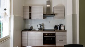 A compact kitchen with light wood cabinets, a stainless steel range hood, a built-in oven, and a window with a view of greenery. - Nonno Luigi by Interhome (Molini di Prelà)