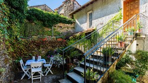 A stone building with a wooden door, a staircase with metal railings, and a table with chairs outside. - Nonno Luigi by Interhome (Molini di Prelà)