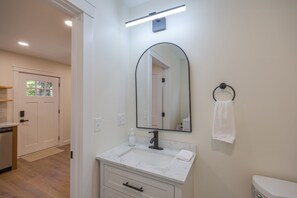 Casa de banho com lavatório branco, espelho, suporte para toalha e sanita.